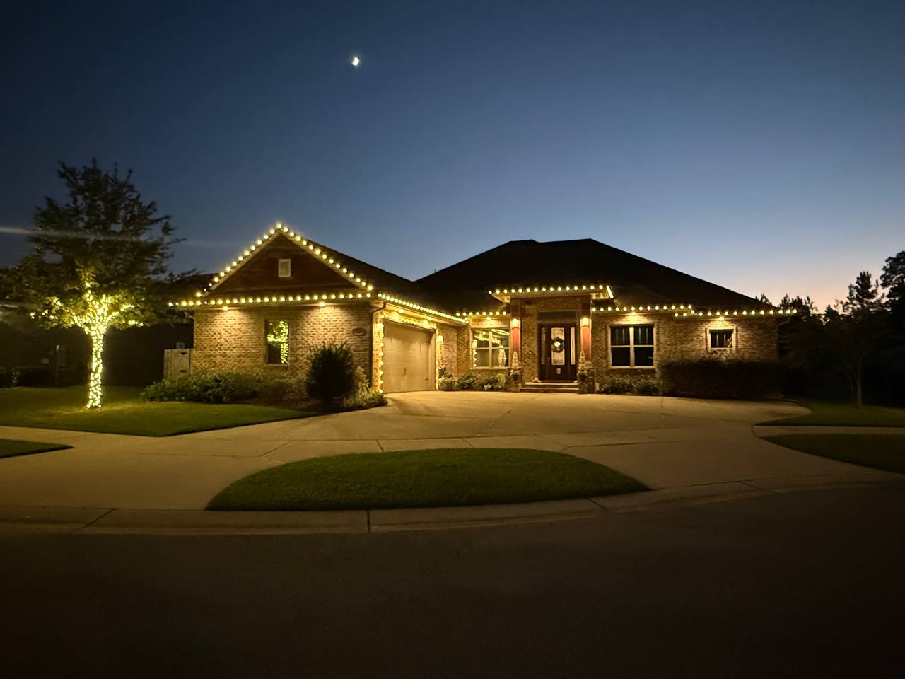 Warm-white roofline Christmas lights and a wrapped tree at Hunt Creek House.